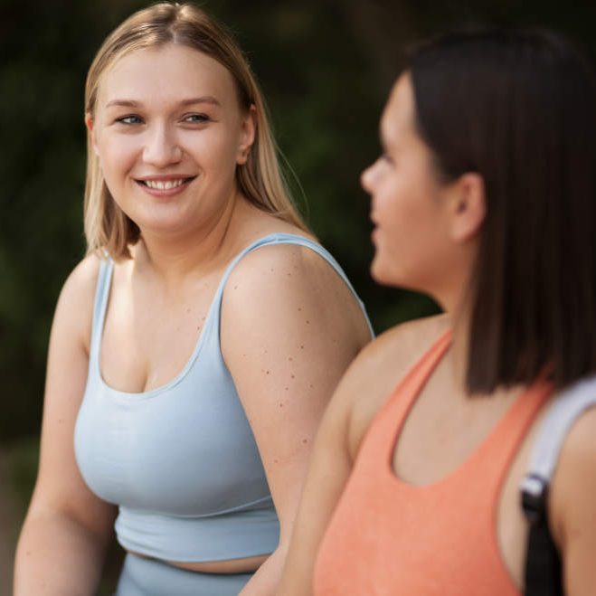 Zwei Frauen in Sportkleidung unterhalten sich lächelnd im Freien.